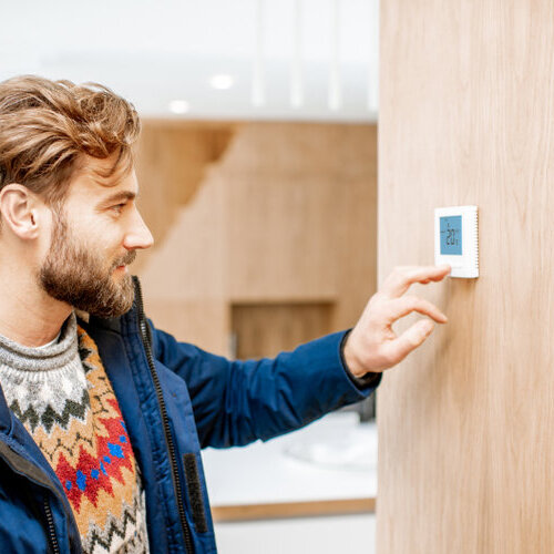 man in a coat turning on the thermostat