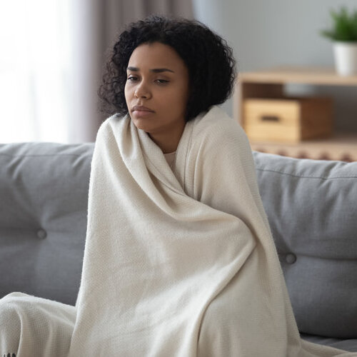 woman in a blanket shivering on a sofa