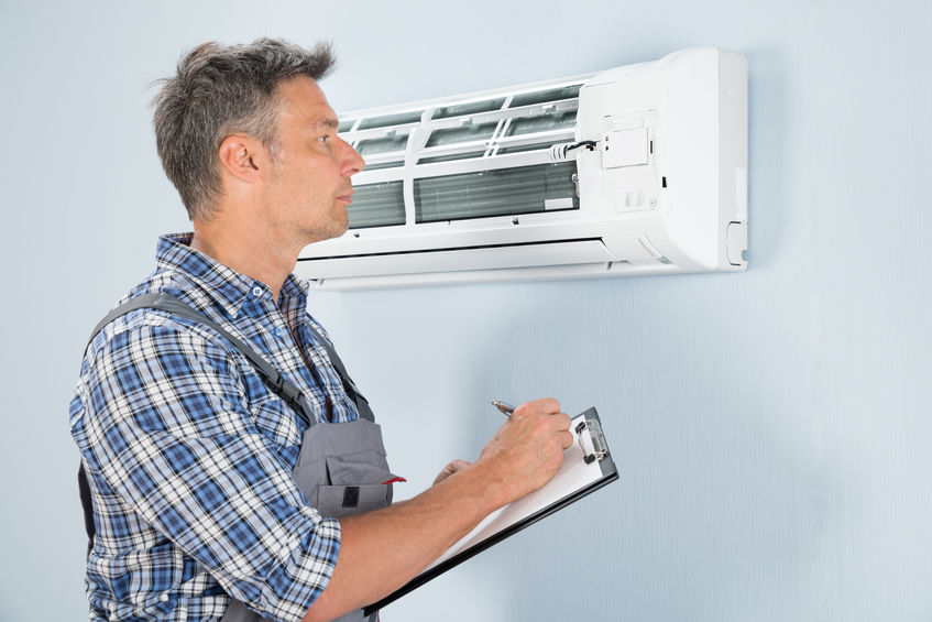 Portrait Of Male Technician Holding Clipboard Looking At Air Conditioner